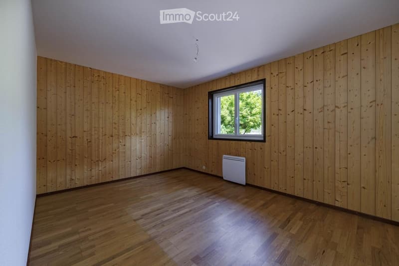 Empty room with wooden walls and floor, a single window, and a white radiator.