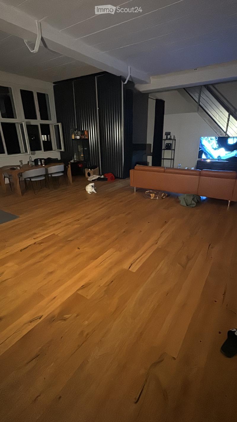 Living room with wooden flooring, a brown leather sofa, a wooden dining table with chairs, a television, and a shelf with various items.