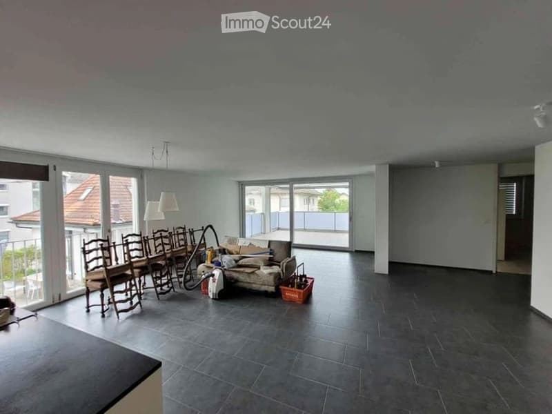 Bright, open living and dining area with large windows and a balcony. Includes a dining table with chairs, a sofa, and a lamp.