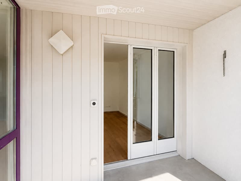 Empty hallway with white paneled walls, a sliding glass door leading to another room, and a wooden floor visible through the door.