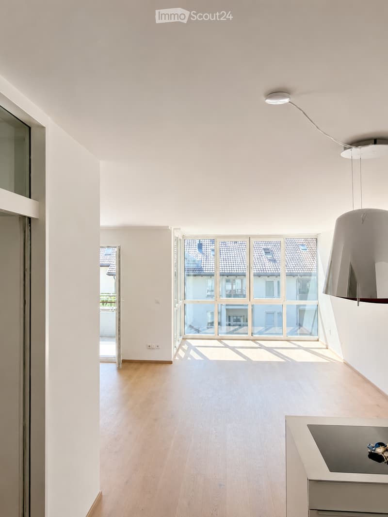 Bright, minimalist room with light wooden flooring, white walls, large windows, and a modern pendant light fixture.