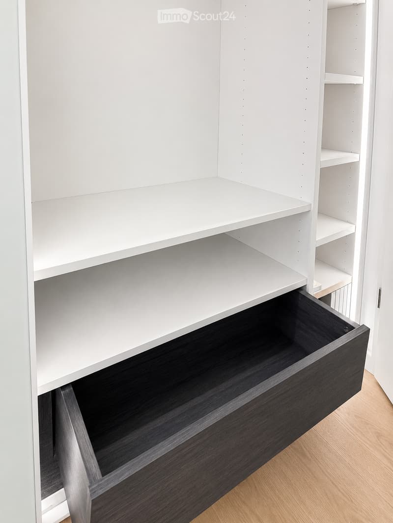 Empty white built-in closet with multiple shelves and a single open drawer, featuring a dark wood finish on the drawer front.