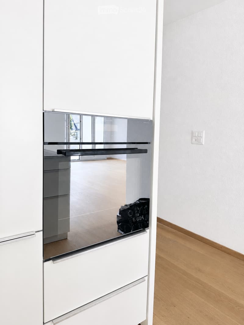 Empty room with white walls, light wooden flooring, and a partially open white cabinet with a mirrored front.