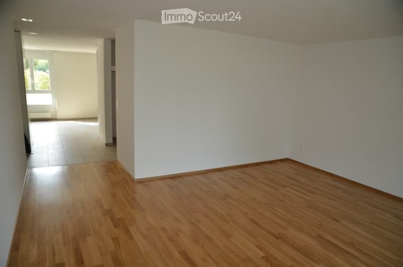 Empty room with wooden flooring and white walls, featuring a large window and a doorway leading to another space.