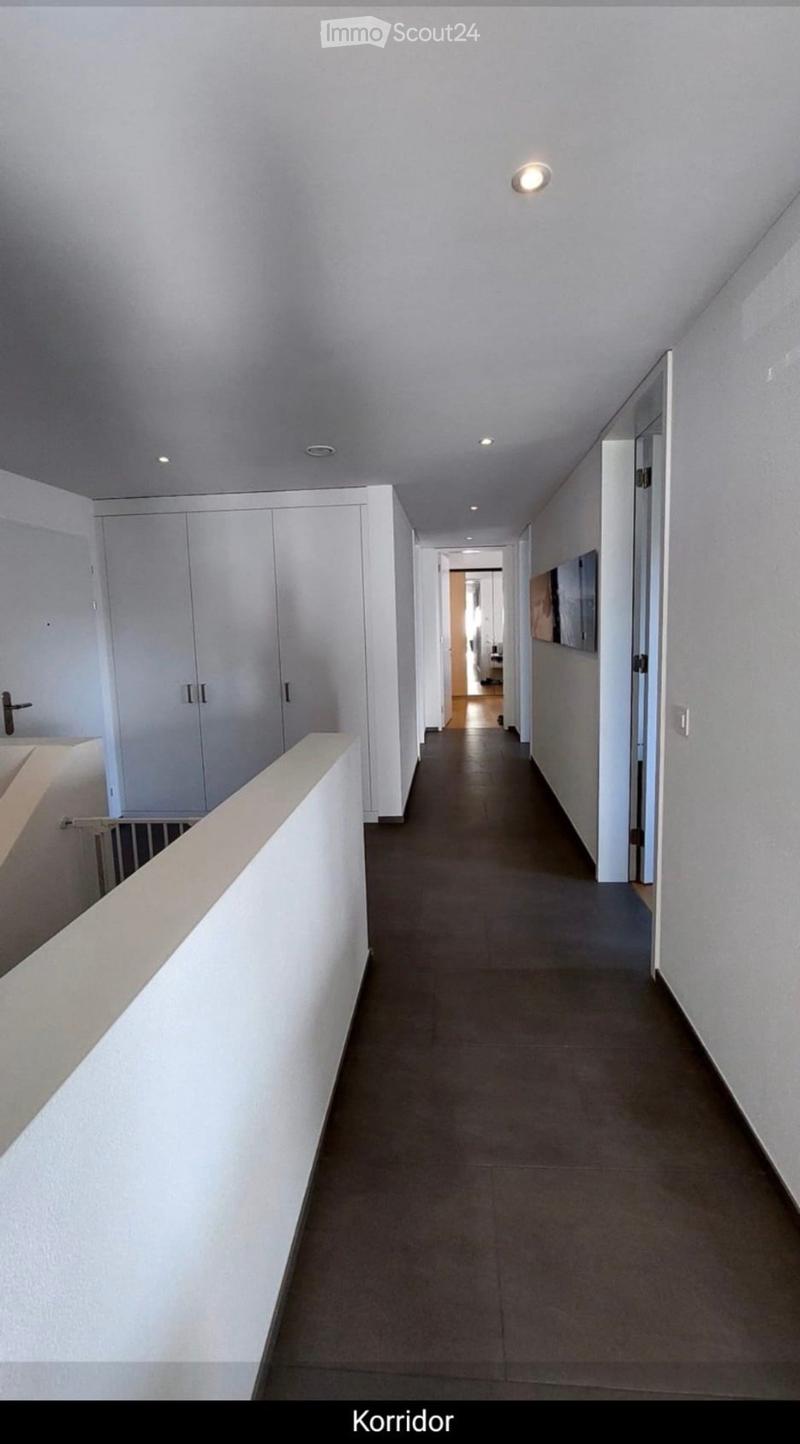 Clean, modern hallway with white walls, gray tiled floor, built-in white storage units, and recessed lighting.