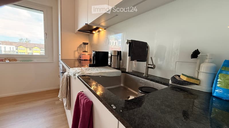 Modern kitchen with granite countertops, stainless steel sink, coffee maker, blender, and various kitchen items on the counter.