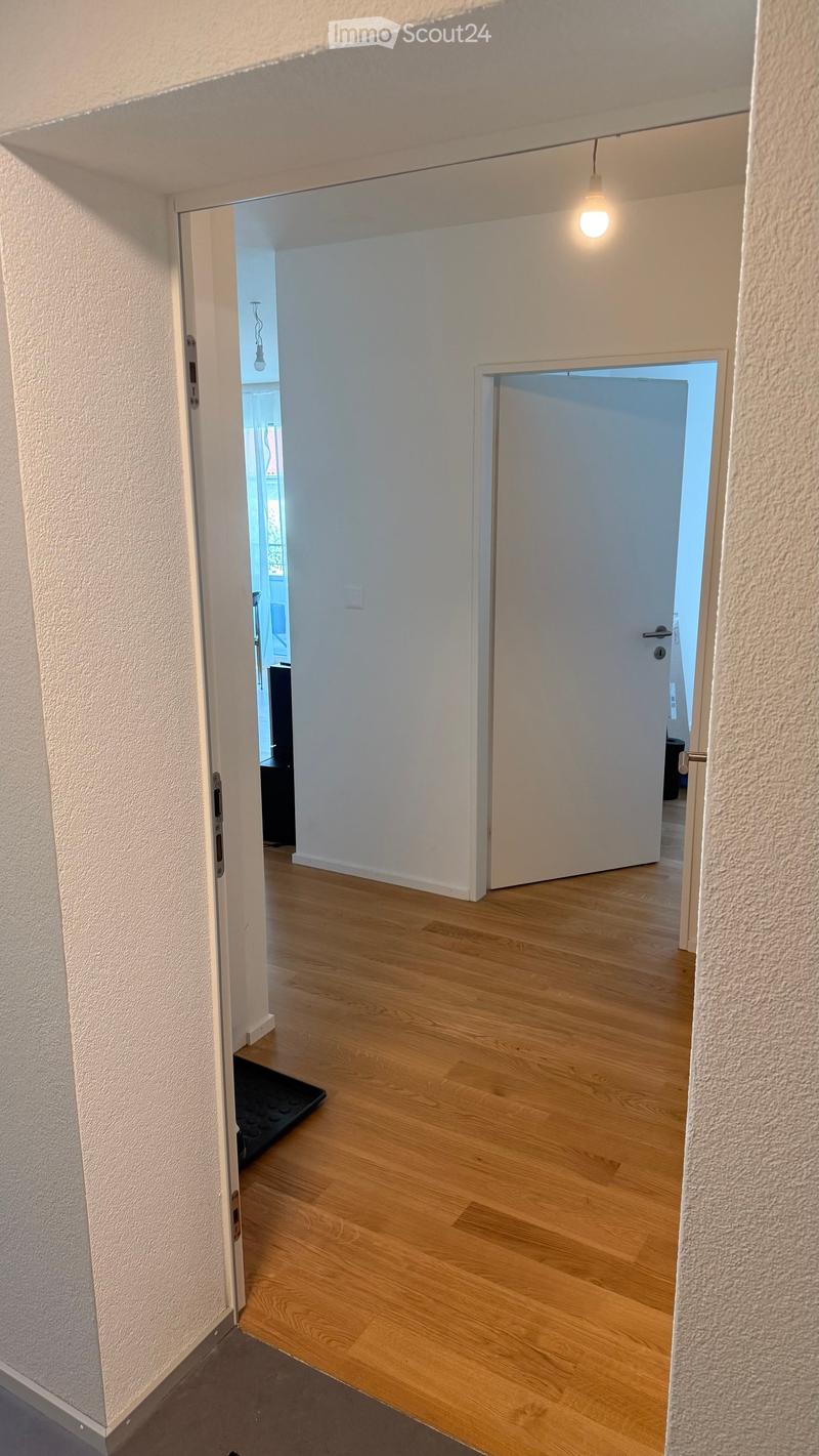 Empty hallway with light wooden flooring, white walls, and two open doors leading to other rooms.