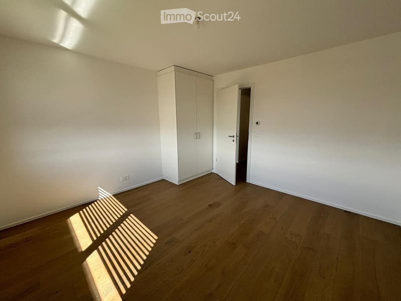 Empty room with wooden flooring, white walls, and a built-in white cabinet. Sunlight streams in from a window, casting shadows on the floor.
