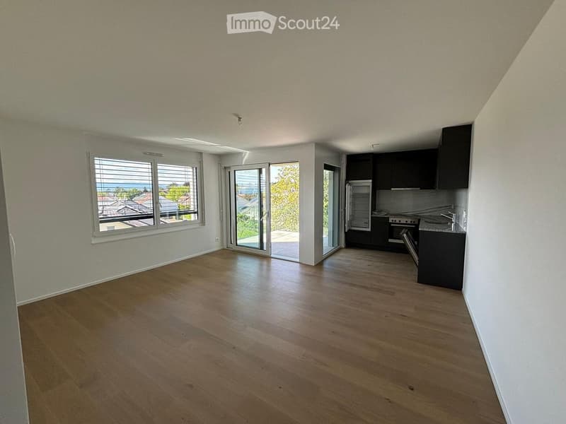 Open-plan unfurnished room with wooden flooring, large windows, and a sliding glass door leading to a balcony.