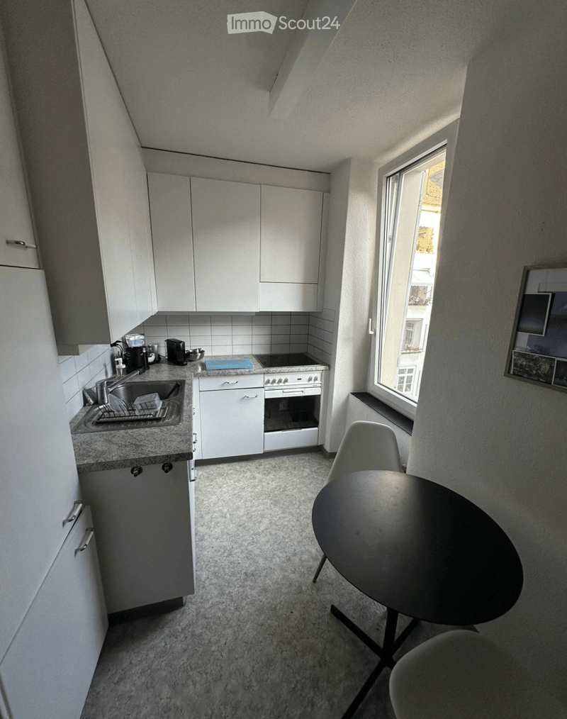 Modern kitchen with white cabinets, a sink, stove, and a small dining area with a round table and chairs.