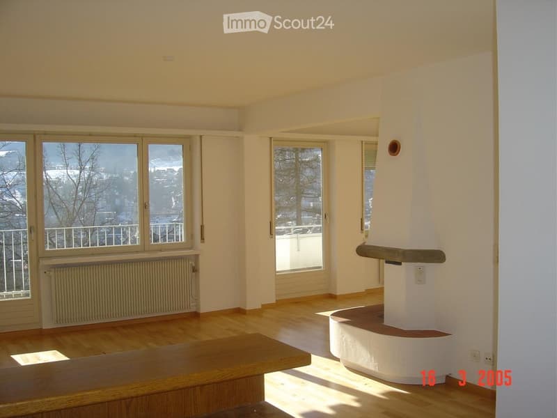 Empty room with wooden flooring, large windows, and a white fireplace structure. No furniture or equipment present.