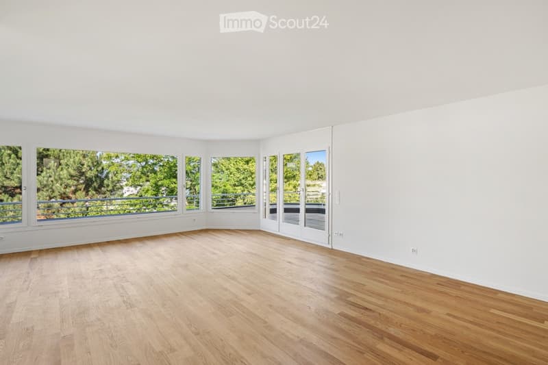 Bright, empty room with wooden flooring, large windows, and sliding glass doors leading to a balcony.