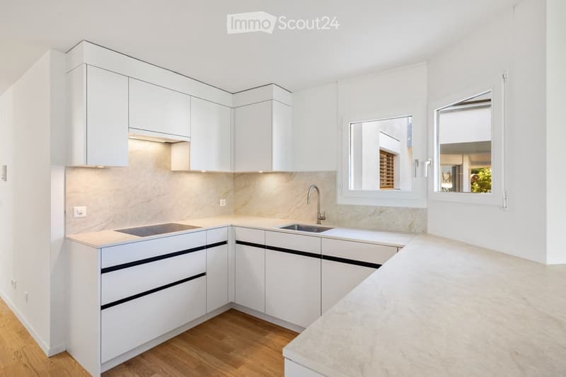 Modern, minimalist kitchen with white cabinets, a marble countertop, and a stainless steel sink.