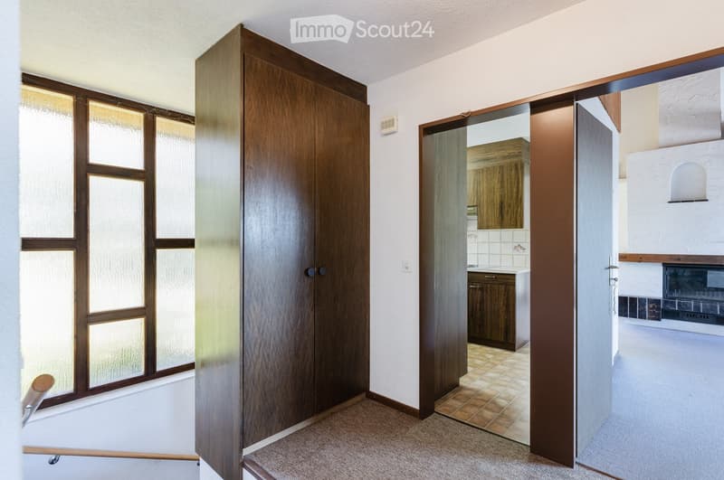 A well-lit hallway with wooden doors, a tiled floor in the adjacent room, and a visible fireplace in the background.