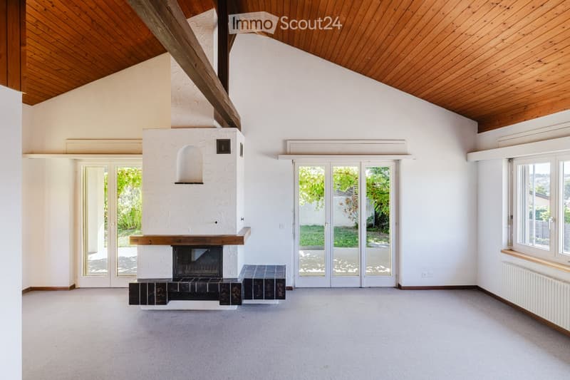 Empty living room with a fireplace, large windows, and sliding glass doors leading to a garden.