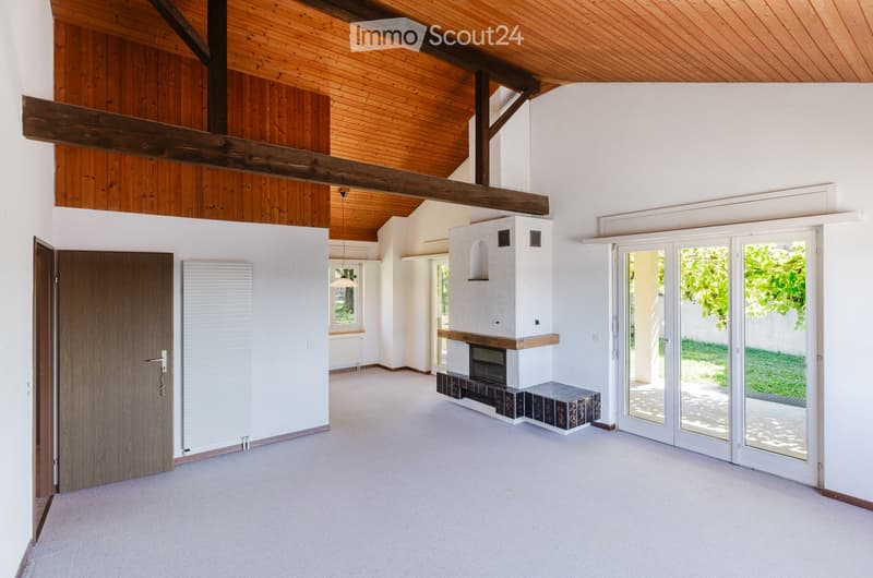 Empty living room with white walls, wooden ceiling beams, large sliding glass doors, and a built-in fireplace.