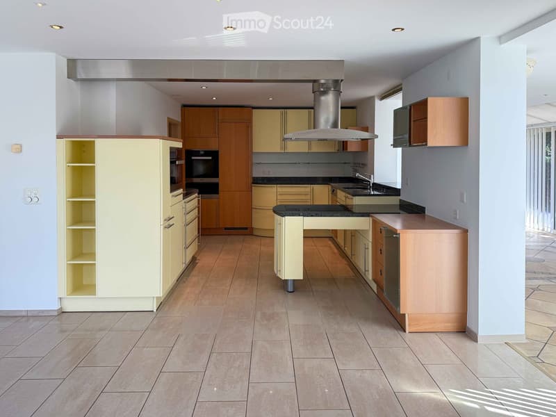Modern kitchen with light-colored cabinets, stainless steel appliances, and a central island. Features include a range hood, sink, and ample storage space.