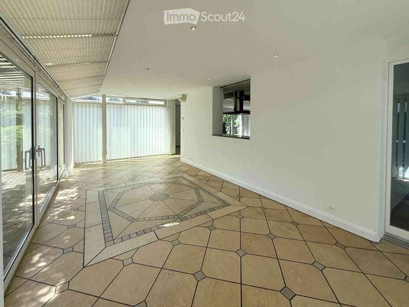 Bright, open hallway with beige tiled flooring and white walls, featuring large glass doors and a skylight above.