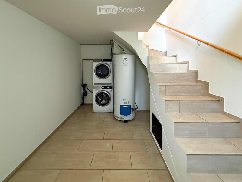 Hallway with tiled floor, staircase leading upwards, and a private washing machine placed against the wall.