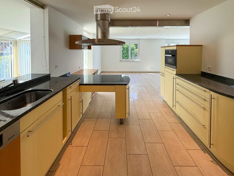 Modern kitchen with light-colored cabinets, granite countertops, and a central island with a built-in sink and range hood.