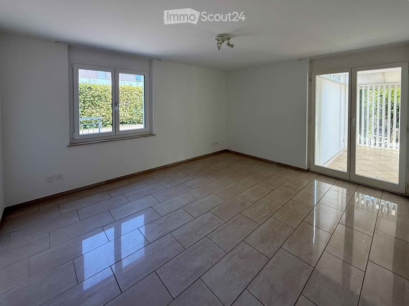 Empty room with tiled floor, white walls, large window, and sliding glass doors leading to a balcony.