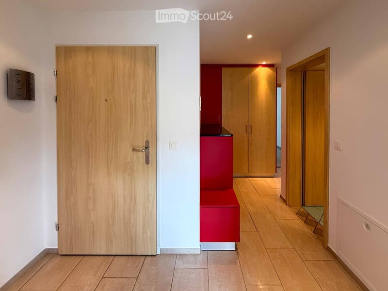 Modern hallway with tiled flooring, white walls, and wooden doors. Features a red bench and built-in wooden cabinets.