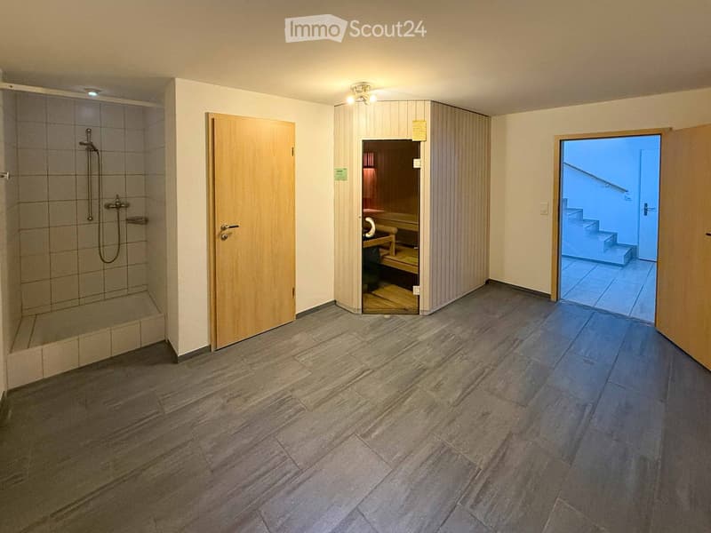 Empty room with tiled floor, shower stall, sauna entrance, and staircase leading upwards.