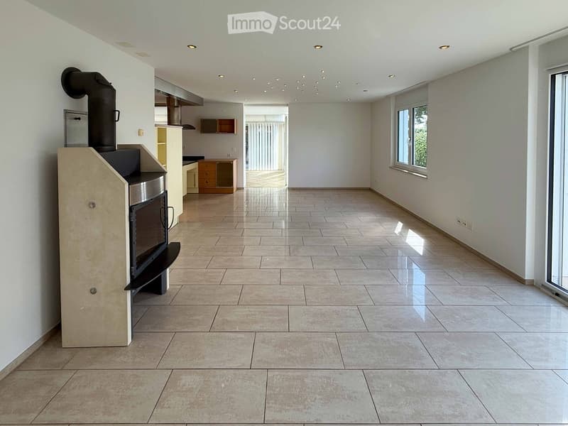 Empty room with tiled floor, white walls, and a fireplace in the corner. The room has large windows and recessed lighting.