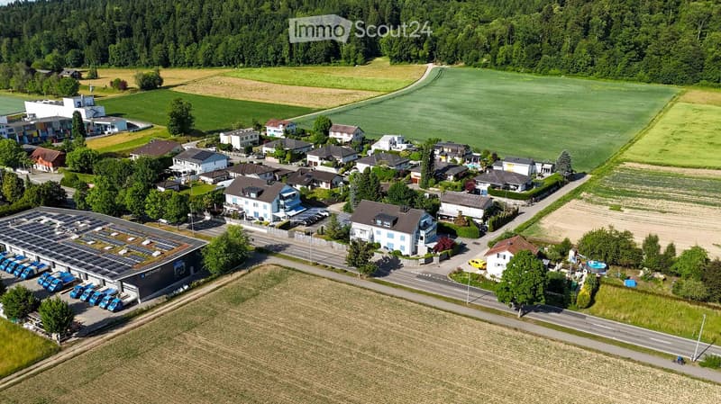 Aerial view of a residential area with multiple houses, a parking lot, and a swimming pool surrounded by greenery and farmland.