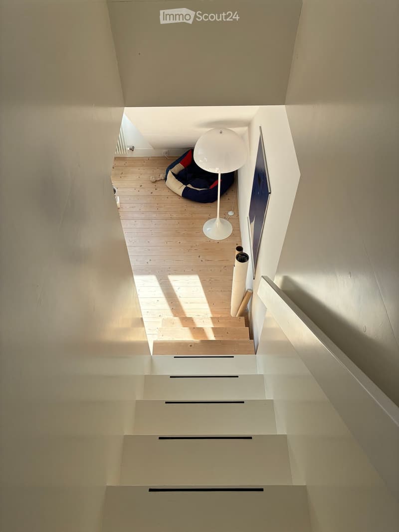 Modern, open-concept hallway with wooden flooring, white walls, and a staircase leading upwards. Features a white spherical lamp, a pet bed, and a TV mounted on the wall.