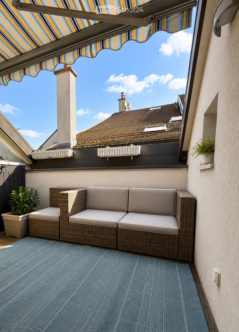 Balcony with wicker sofa, ottoman, potted plants, and a striped awning.