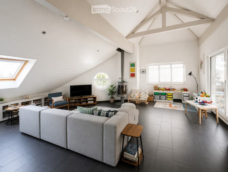 Modern living room with a high, slanted ceiling, large windows, and skylight. Features a grey sectional sofa, coffee table, TV stand, fireplace, and children's play area with a small table and chairs.