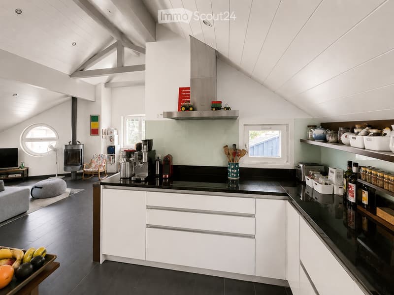 Open-plan living and kitchen area with white cabinets, black countertops, a fireplace, and a sofa. The space features a modern design with ample natural light from large windows and a skylight.