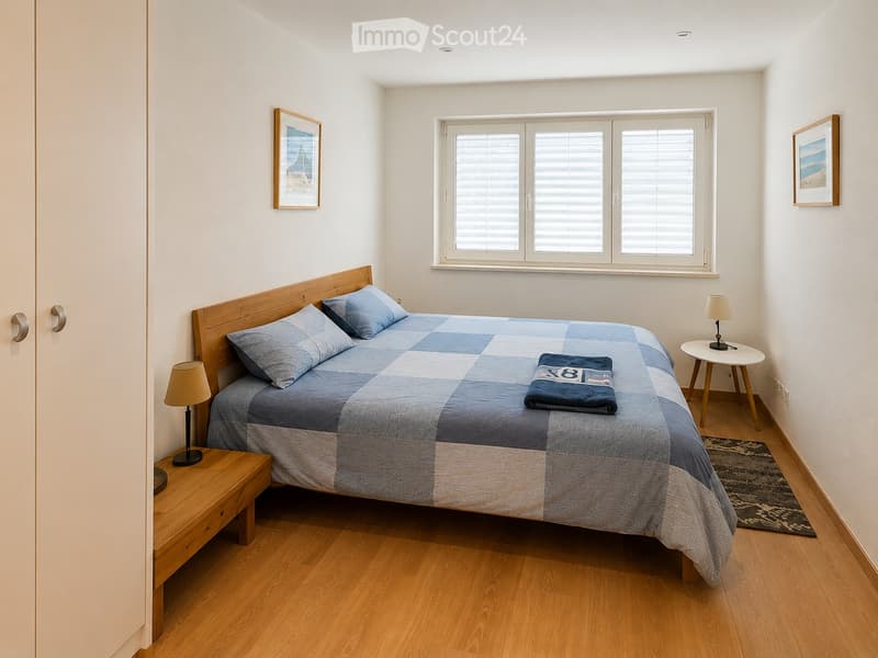 Cozy bedroom with a wooden bed, blue and white checkered quilt, two nightstands with lamps, and framed pictures on the walls.