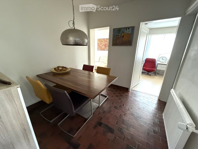 Dining area with a wooden table, chairs, and a clock visible in the adjacent room.