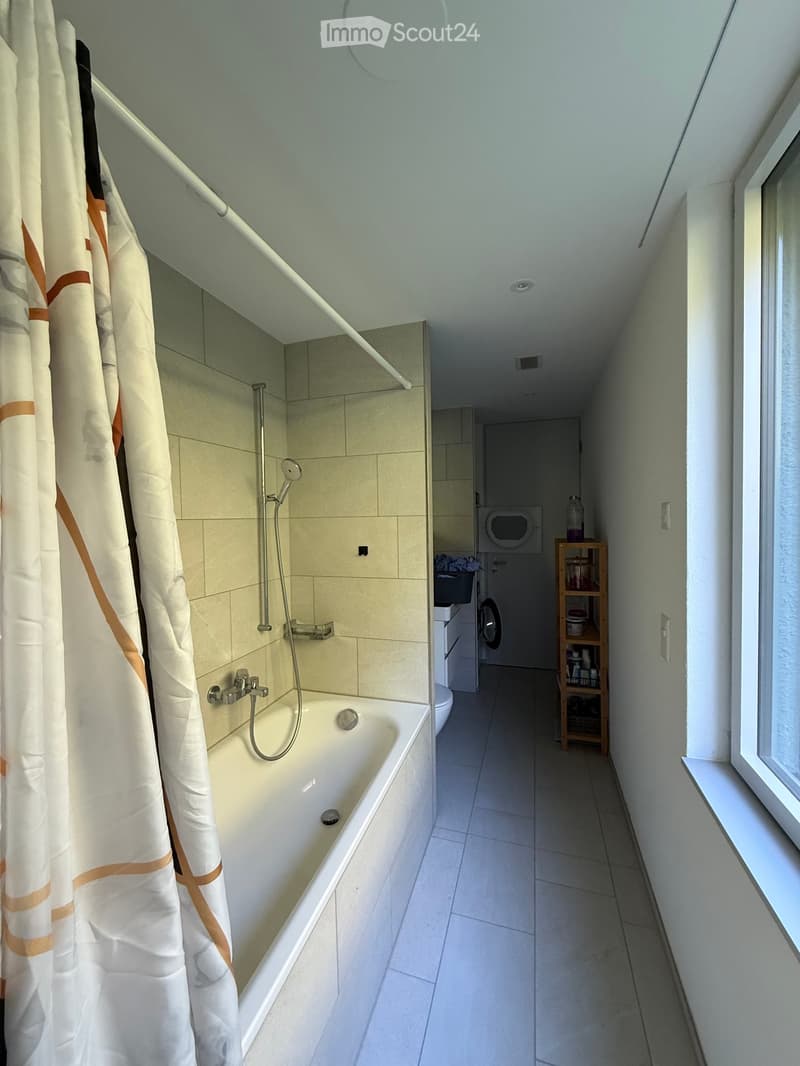 Bathroom with a bathtub, showerhead, and a washing machine in the adjacent area.
