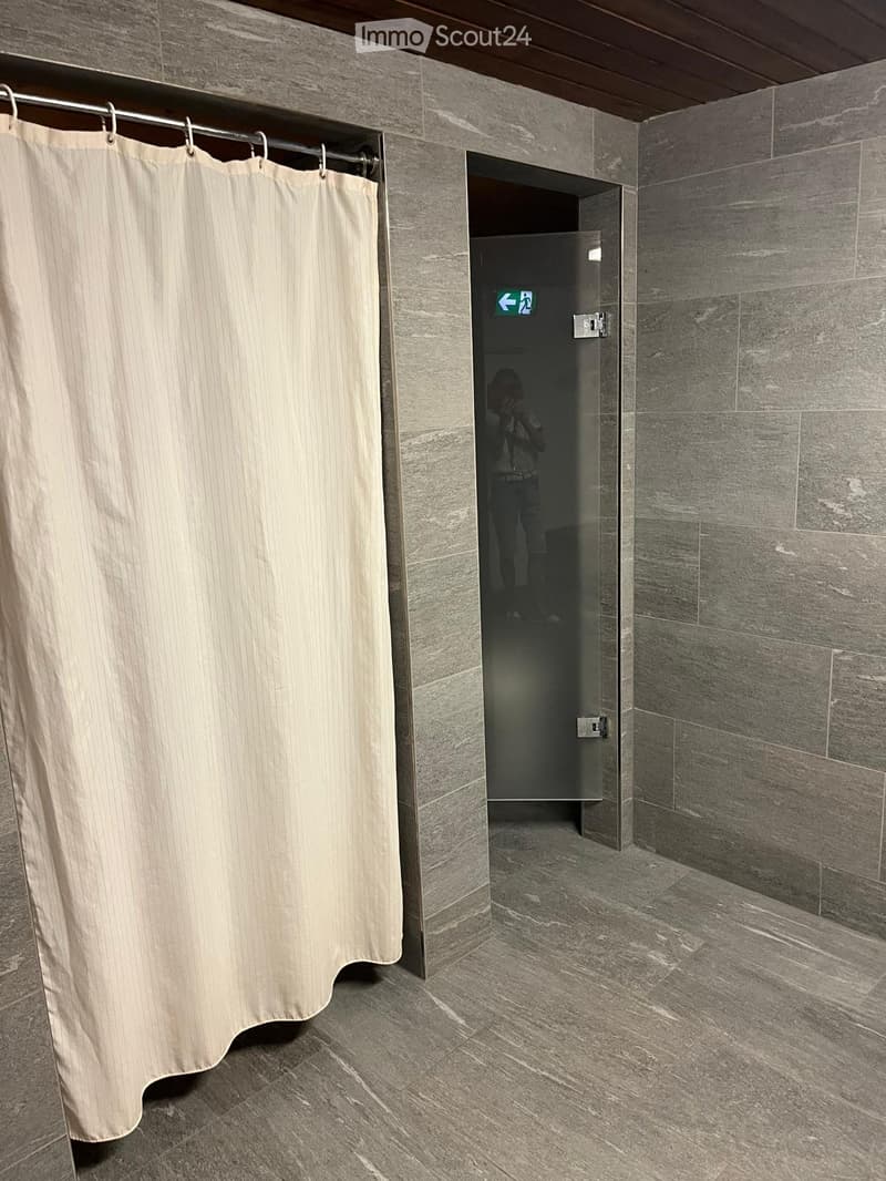 Modern bathroom with grey tiled walls and floor, featuring a shower curtain and a glass-enclosed shower area.