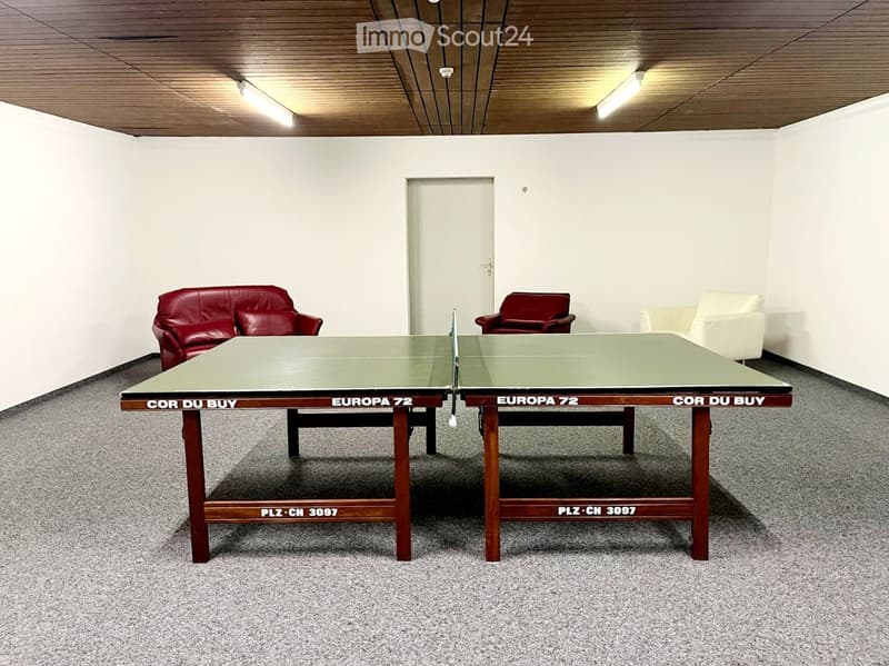 A room with a table tennis table, two red chairs, and a white sofa.