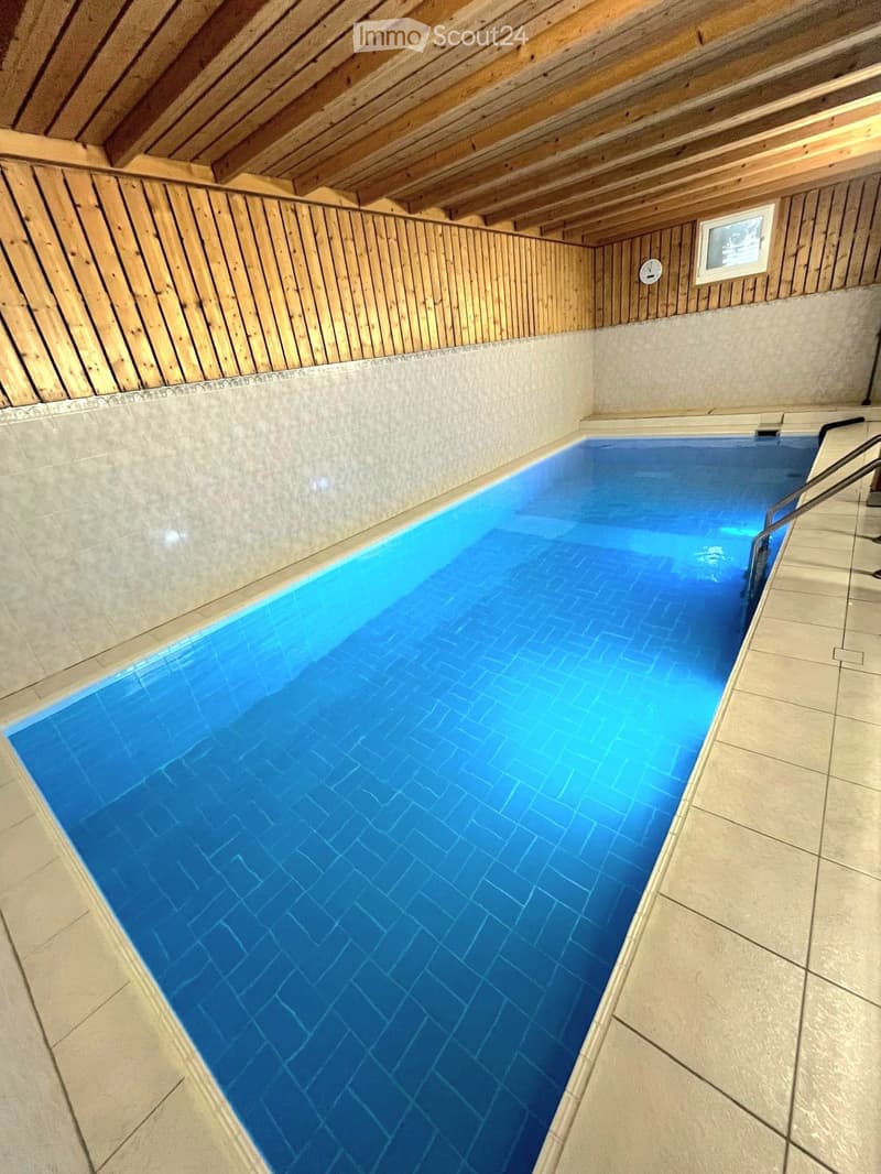 Indoor swimming pool with wooden ceiling and tiled walls, featuring a small window and a metal handrail on one side.