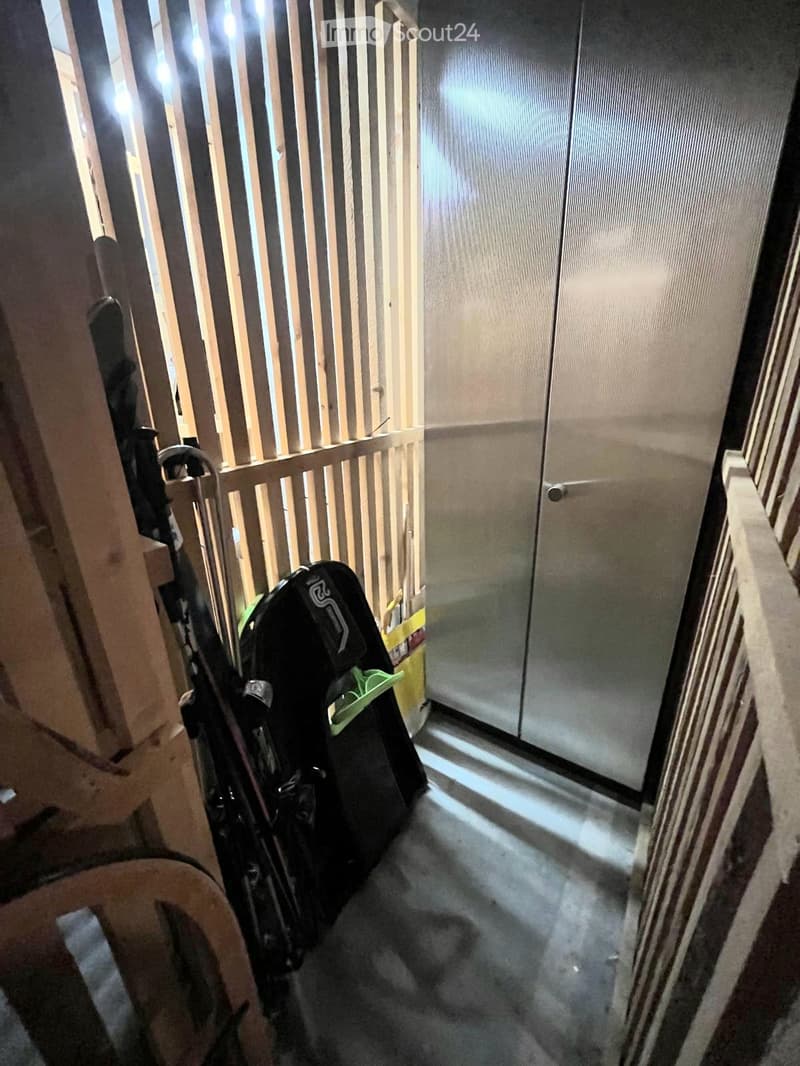 A narrow hallway with a wooden railing on one side and a glass door at the end. A stroller is parked against the railing.