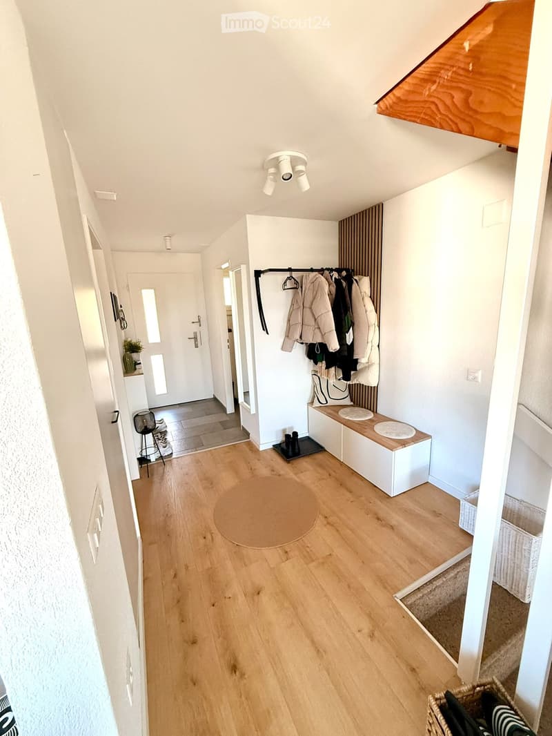 Bright hallway with wooden flooring, built-in bench with storage, coat rack, and small round rug. Features modern lighting and white walls.