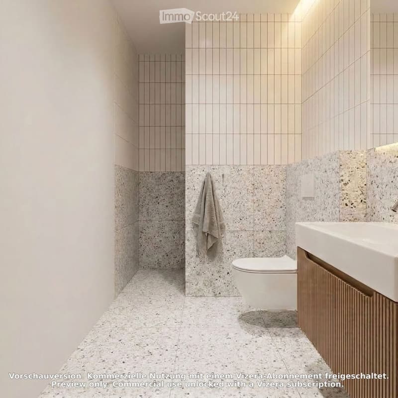 Modern bathroom with light-colored tiles, a toilet, a sink with a wooden cabinet, and a towel hanging on the wall.