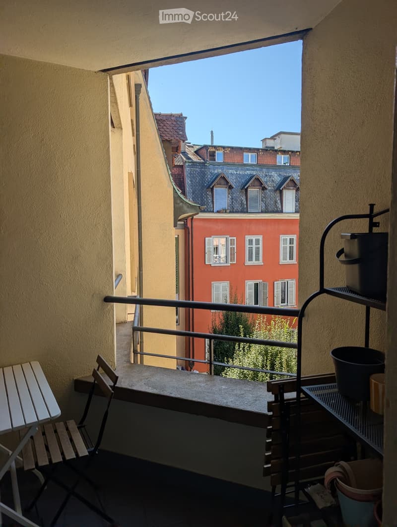 Balcony with a view of a cityscape, featuring a chair, table, and potted plants.