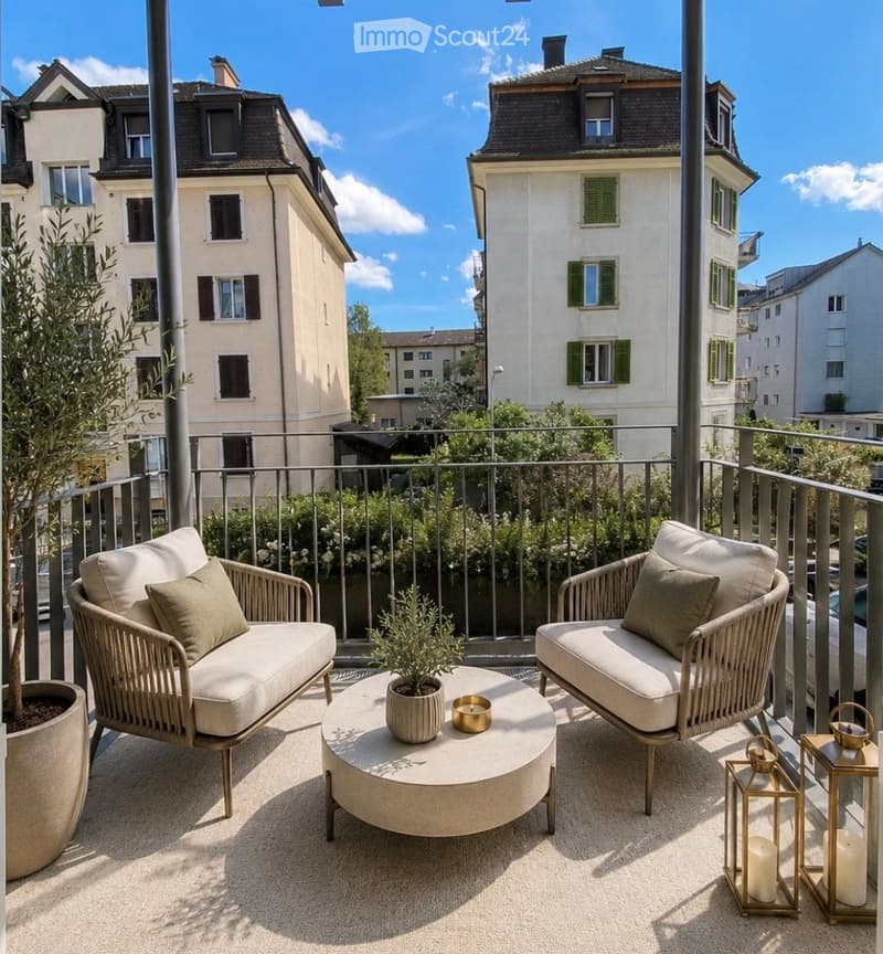 A modern balcony with two wicker sofas, a round coffee table, potted plants, and lanterns, overlooking a cityscape with classic buildings.