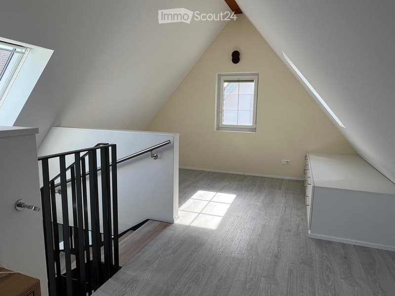 Bright, open hallway with wooden flooring, white walls, and a modern metal railing leading to a staircase. Features a skylight window and a smaller window on the wall.