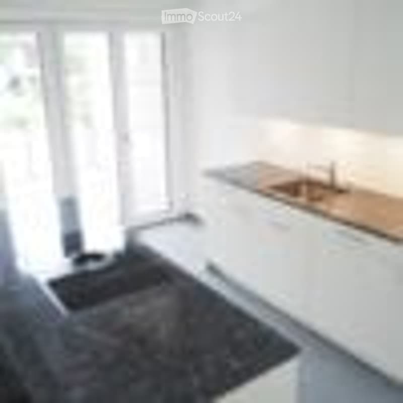 Bright, minimalist kitchen with white cabinetry, a wooden countertop, and a black rug on the floor. The space is completely empty, with no appliances or furniture visible.