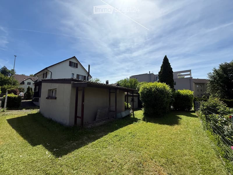 A well-maintained garden area with a small shed, green lawn, and surrounding trees and bushes.