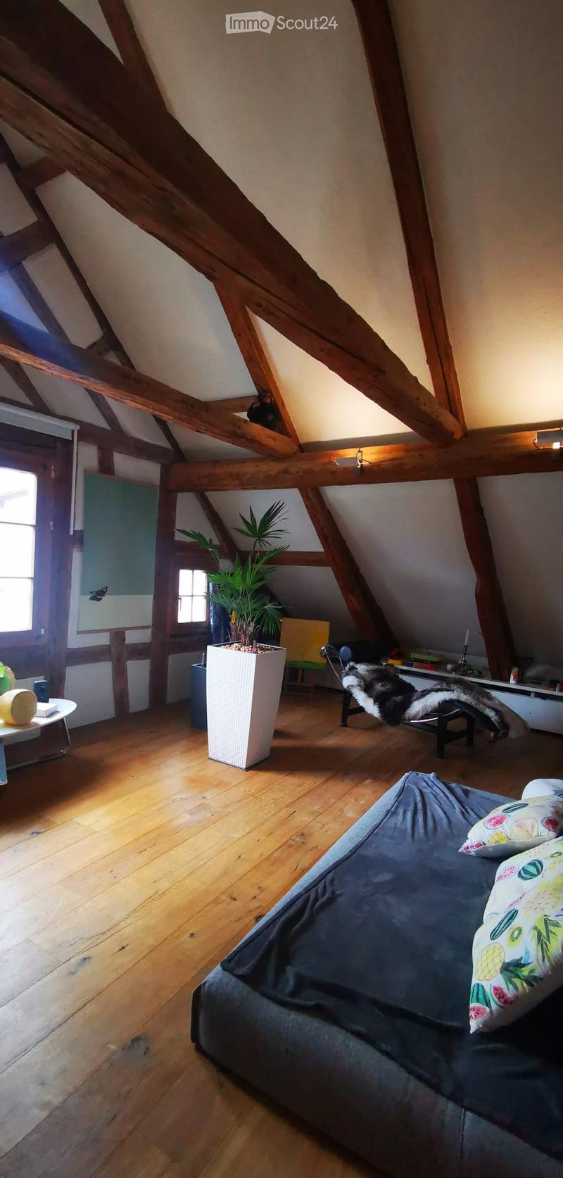 Cozy attic room with wooden beams, exposed wooden floor, sofa, small table, chair, and a potted plant.