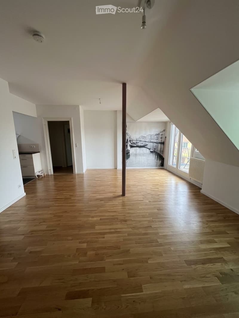 Empty room with wooden flooring, white walls, large windows, and a mural of a canal scene. No furniture or equipment present.