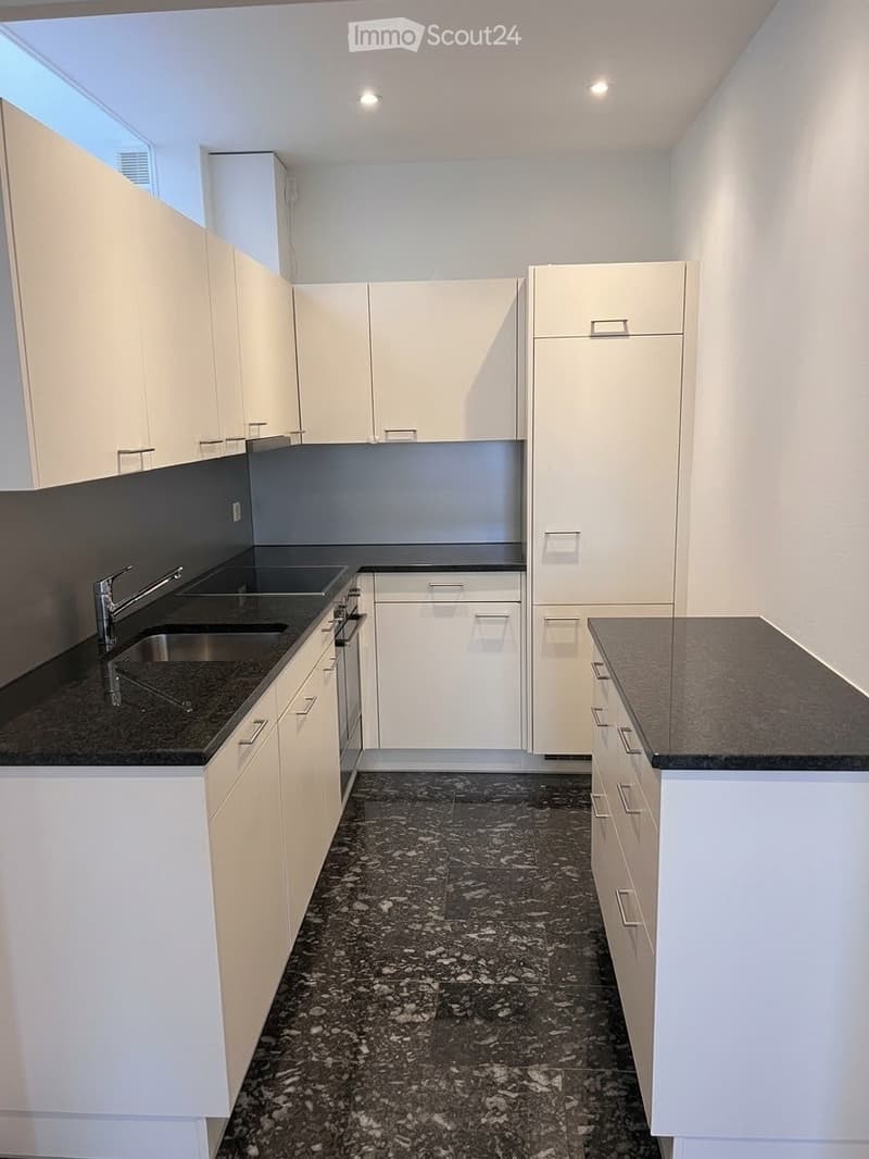 Modern kitchen with white cabinets, dark countertops, and a black granite floor.
